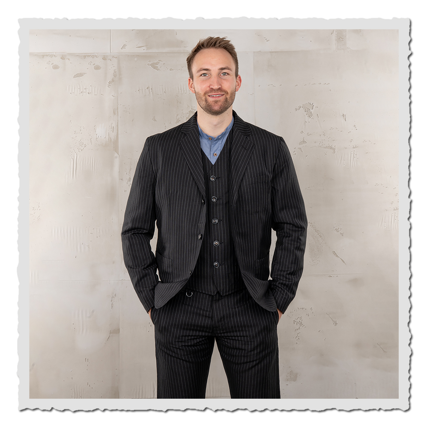 Model trägt schwarzes Nadelstreifen-Sakko mit Weste und Hose, Frontansicht vor hellem Studiohintergrund.